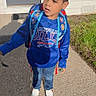 child, boy, backpack, blue_hoodie, jeans, sneakers, outdoor, sidewalk, grass, house, door, window, sunlight, shadow, curly_hair, casual_clothing, daylight, young, person, standing