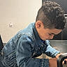 Xadiel Estévez is registered to the contest to win money with this photo: child, boy, curly_hair, denim_jacket, indoor, glass_table, focused, casual_clothing, modern_interior, young, cute, curious, hairstyle, leaning, table, wooden_floor, black_chair, portrait, side_view, person