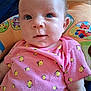 baby, infant, child, pink_onesie, bee_pattern, blue_eyes, cushion, plush_toy, cute, portrait, indoor, closeup, smiling_bees, clothing, person, face, young_child, soft_toys, colorful, resting