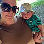 Elliott joined the competition — help win amazing prizes! woman, baby, outdoor, sunglasses, hat, greenery, sunlight, portrait, child, person, casual_clothing, nature, smile, holding, face, headwear, summer, daylight, park, cute