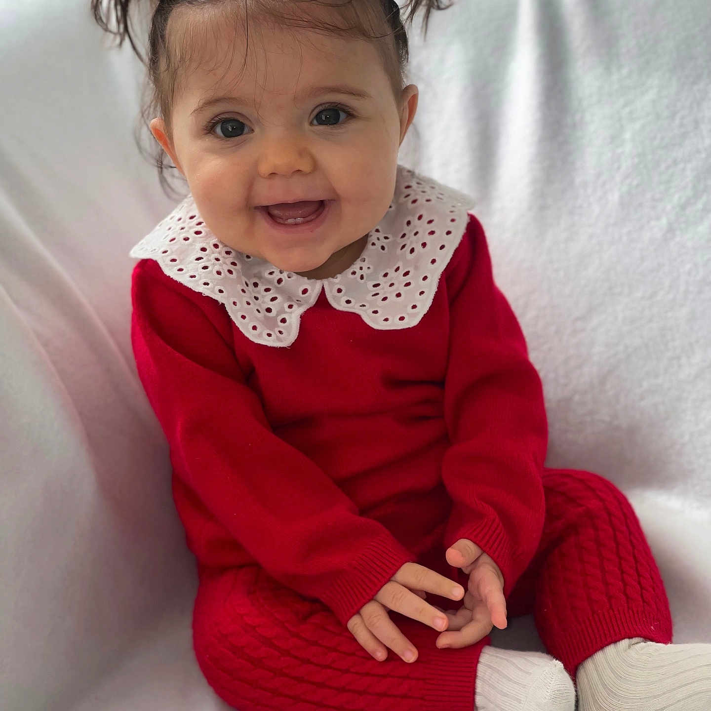Esmée a rejoint le concours — aidez-le/la à gagner de superbes lots ! baby, blanket, child, cozy, cute, expression, face, hands, happy, indoor, infant, knitwear, pigtails, portrait, red_clothing, sitting, smiling, sock, white_collar, young_child