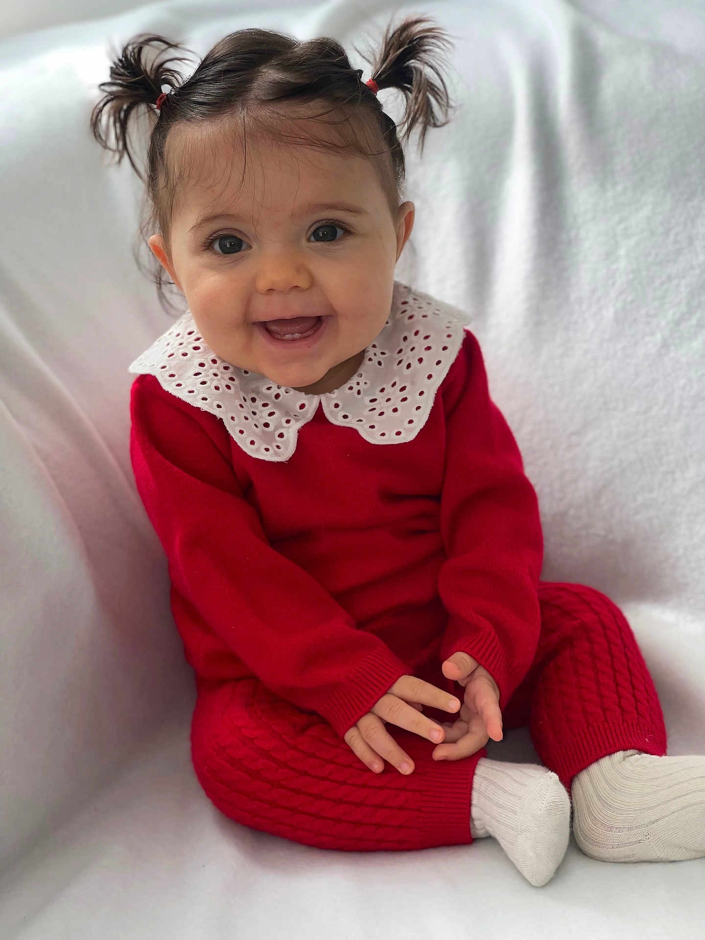 Esmée a rejoint le concours — aidez-le/la à gagner de superbes lots ! baby, child, smiling, red_clothing, white_collar, pigtails, sitting, happy, cute, portrait, indoor, cozy, sock, knitwear, infant, face, hands, blanket, young_child, expression