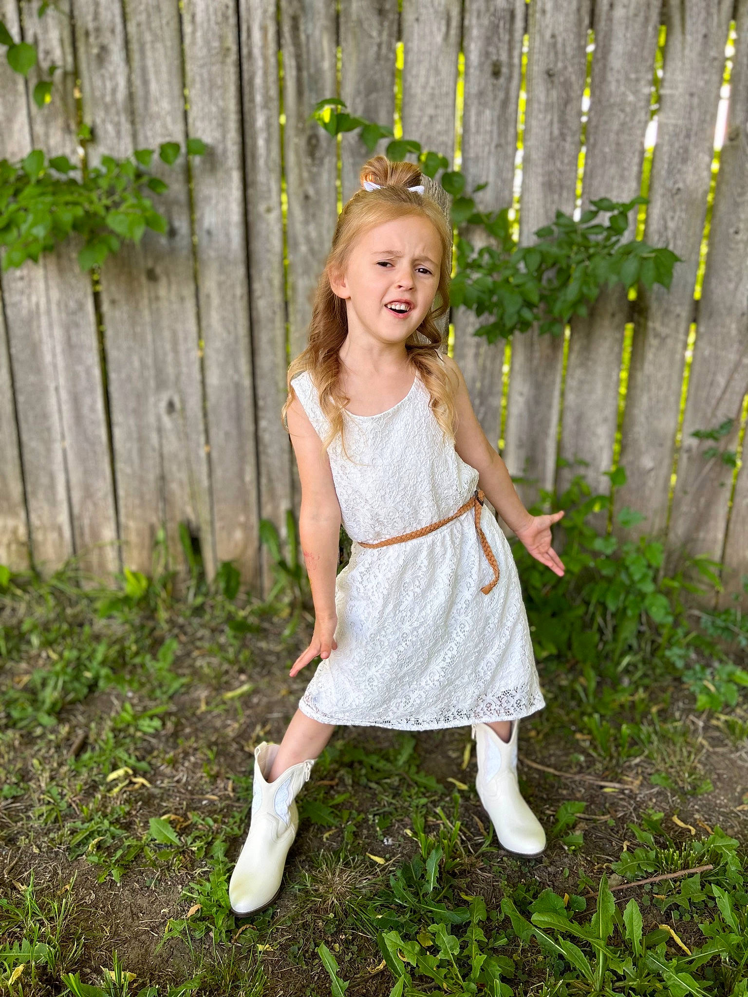 Brooklynn is registered to the contest to win money with this photo: blond, brown_hair, child, day_dress, dress, fawn, fence, formal_wear, grass, grass_family, happy, head, human_leg, long_hair, pattern, people_in_nature, person, plant, sleeve, toddler