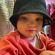 Déborah a rejoint le concours — aidez-le/la à gagner de superbes lots ! toddler, child, hat, black_hat, hello_kitty, orange_sweater, indoor, face, portrait, young_child, cute, knit_hat, clothing, crocheted_blanket, wooden_furniture, person, baby, smiling, warm_lighting, closeup