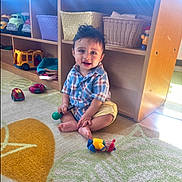 Oliver joined the competition — help win amazing prizes! basket, carpet, child, clothing, colorful, cute, floor, furniture, hair, indoors, natural_light, person, play, playroom, plush_toy, sitting, smiling, toddler, toy, wooden_shelf