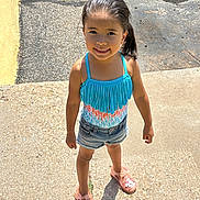 Malia is registered to the contest to win money with this photo: child, girl, smiling, outdoor, sunlight, swimsuit, blue, denim_shorts, pink_sandals, wet_hair, pavement, shadow, summer, casual_clothing, standing, happy, portrait, daylight, fringe, playful