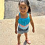 child, girl, smiling, outdoor, sunlight, swimsuit, blue, denim_shorts, pink_sandals, wet_hair, pavement, shadow, summer, casual_clothing, standing, happy, portrait, daylight, fringe, playful