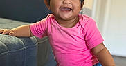 Zunairah joined the competition — help win amazing prizes! baby, blue_pants, carpet, child, couch, eyes, face, furniture, hair_bows, hand_on_couch, happy, indoors, living_room, pigtails, pink_shirt, playful, portrait, smiling, standing, toddler