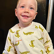 Esteban participe au concours pour gagner de l'argent avec cette photo : background_blur, blond_hair, blue_eyes, casual_clothing, child, clothing_pattern, crocodile_pattern, cute, face, fashion, happy, head_and_shoulders, indoor, long_sleeves, person, playful, portrait, smiling, sweater, young_child