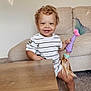 Adrian joined the competition — help win amazing prizes! toddler, child, smiling, curly_hair, toy, mermaid_doll, couch, living_room, table, carpet, family_photos, wall, happy, casual_clothing, indoor, person, foot, shorts, striped_shirt, home