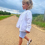 Louis participe au concours pour gagner de l'argent avec cette photo : child, blonde_hair, white_shirt, striped_shorts, sandals, walking, road, country_road, outdoor, grass, cloudy_sky, rural, nature, side_view, person, summer, casual_clothing, young_child, portrait, daytime