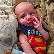 Conrad is registered to the contest to win money with this photo: baby, infant, blanket, superman, clothing, cute, face, hand, soft, cozy, child, portrait, sleeping_area, bed, expression, skin, newborn, warm, comfort, lying_down