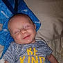 baby, smiling, sleeping, blue_blanket, striped_shirt, text_on_clothing, indoor, infant, closeup, peaceful, child, cute, soft_texture, bed, pillow, human, portrait, baby_clothes, resting, happy