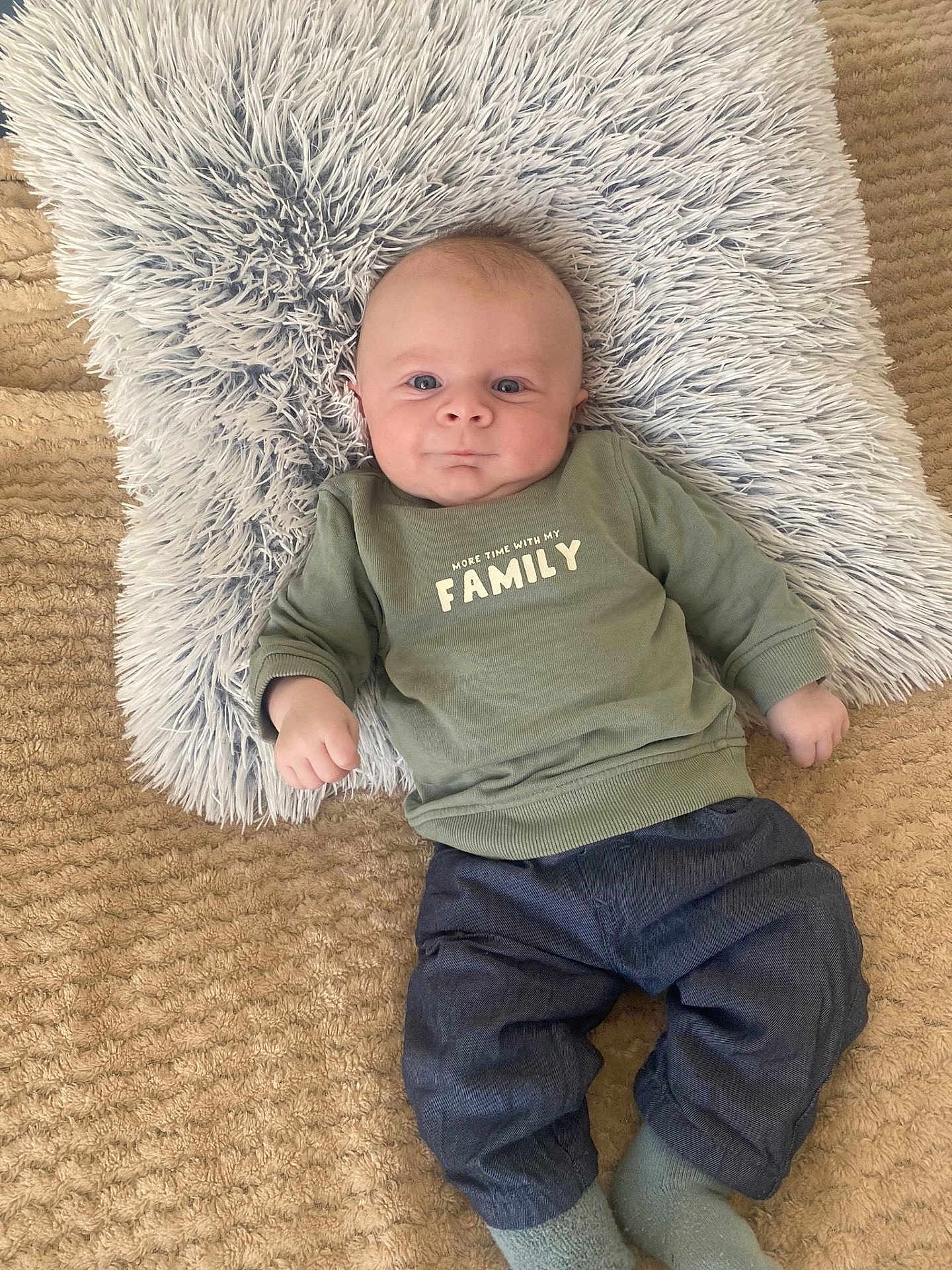 Léo participe au concours pour gagner de l'argent avec cette photo : baby, infant, child, pillow, shaggy_pillow, rug, carpet, sweatshirt, family_text, shirt, pants, denim_pants, socks, blue_eyes, portrait, lying_down, cozy, indoor, cute, smiling