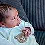 baby, infant, child, soft_clothing, teddy_bear_patch, couch, cushion, portrait, face, hand, indoors, cozy, cute, young_child, person, seated, looking_away, warm, comfortable, closeup