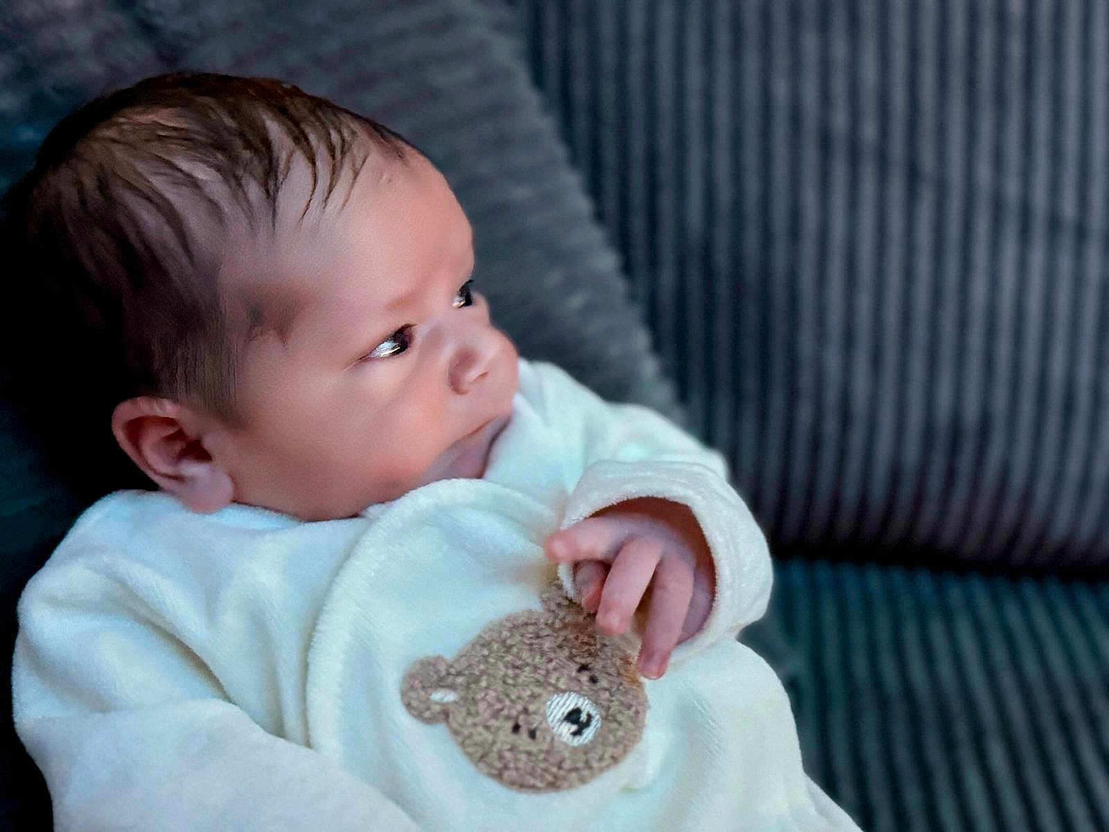 Maylone a rejoint le concours — aidez-le/la à gagner de superbes lots ! baby, infant, child, soft_clothing, teddy_bear_patch, couch, cushion, portrait, face, hand, indoors, cozy, cute, young_child, person, seated, looking_away, warm, comfortable, closeup