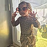 child, sunglasses, leopard_print, fashion, window, curtains, sunlight, indoor, pose, standing, tile_floor, bracelet, long_sleeves, pants, confident, young, person, cute, accessories, daylight