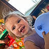 child, toddler, balloon, smile, happy, face, hair, indoors, blanket, colorful, toy, doll, playful, person, purple_clothing, hand, window, daylight, closeup, portrait
