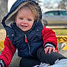 child, toddler, smiling, jacket, hood, outdoor, winter_clothing, blue_eyes, red_sleeves, black_pants, white_shoes, hand, face, blurred_background, car, tree, yellow_surface, daylight, portrait, happy