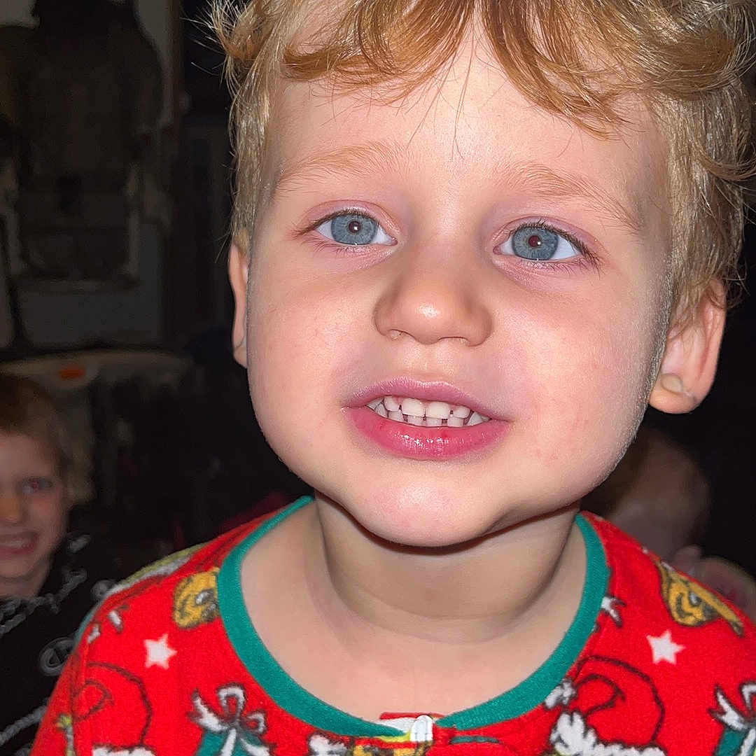 Eli joined the competition — help win amazing prizes! child, smiling, pajamas, red_clothing, blue_eyes, blond_hair, face, indoor, holiday, grinch, patterned_clothing, young_child, portrait, cute, happy, person, closeup, expression, christmas, family