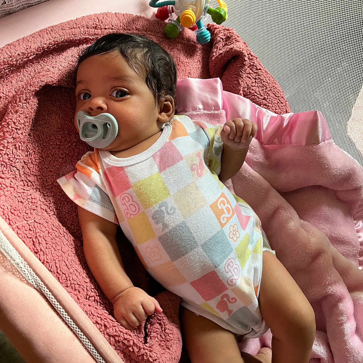 Cherish is registered to the contest to win money with this photo: baby, baby_clothing, blanket, child, colorful, cozy, cute, indoor, infant, lying_down, newborn, onesie, pacifier, pink, playpen, portrait, relaxed, resting, soft_toy, toy