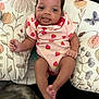 baby, infant, child, smiling, onesie, hair_bow, pillow, floral_pattern, cute, tongue_out, relaxed, indoor, soft_toy_support, pink_clothing, legs, feet, hand, person, happy, closeup