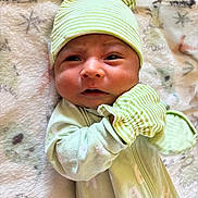 Grayson is registered to the contest to win money with this photo: baby, infant, green_hat, mittens, striped_clothing, blanket, soft_texture, cute, newborn, lying_down, indoors, face, headgear, sleepwear, child, young_baby, warm_clothing, expression, portrait, cozy