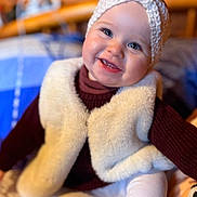Angelina participe au concours pour gagner de l'argent avec cette photo : baby, bed, blanket, blue_eyes, child, cozy, cute, face, happy, indoor, infant, knit_hat, portrait, sitting, smiling, soft_lighting, toddler, vest, warm_clothing, wooden_background