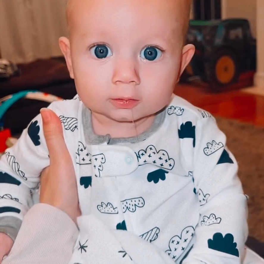 Briggs is registered to the contest to win money with this photo: baby, bodypart, clothing, electronics, face, finger, frown, hand, head, newborn, pajamas, person, photography, portrait, sad, screen, sitting, t_shirt, toy, wrist