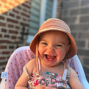 Victoire a rejoint le concours — aidez-le/la à gagner de superbes lots ! baby, bucket_hat, child, closeup, cute, dress, face, hands, happy, hat, high_chair, infant, joyful, laughing, outdoor, patterned, seat, smiling, sunlight, young_child