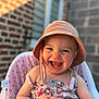 baby, bucket_hat, child, closeup, cute, dress, face, hands, happy, hat, high_chair, infant, joyful, laughing, outdoor, patterned, seat, smiling, sunlight, young_child