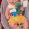 baby, child, infant, portrait, sitting, bouncer, toy, dinosaur, stuffed_animal, smiling, face, indoors, clothing, checkered_shorts, bib, chair, nursery, blanket, safe, photography