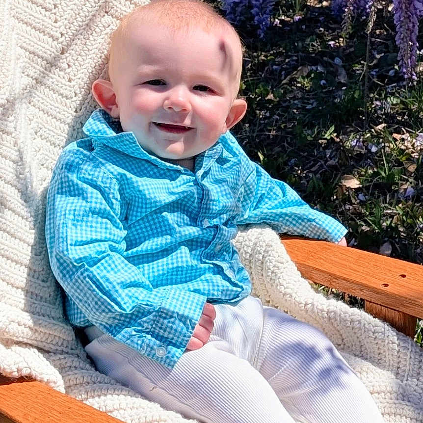 Grayson is registered to the contest to win money with this photo: baby, chair, clothing, cushion, face, flower, furniture, grass, happy, head, homedecor, outdoors, pants, person, photography, plant, portrait, purple, quilt, sitting