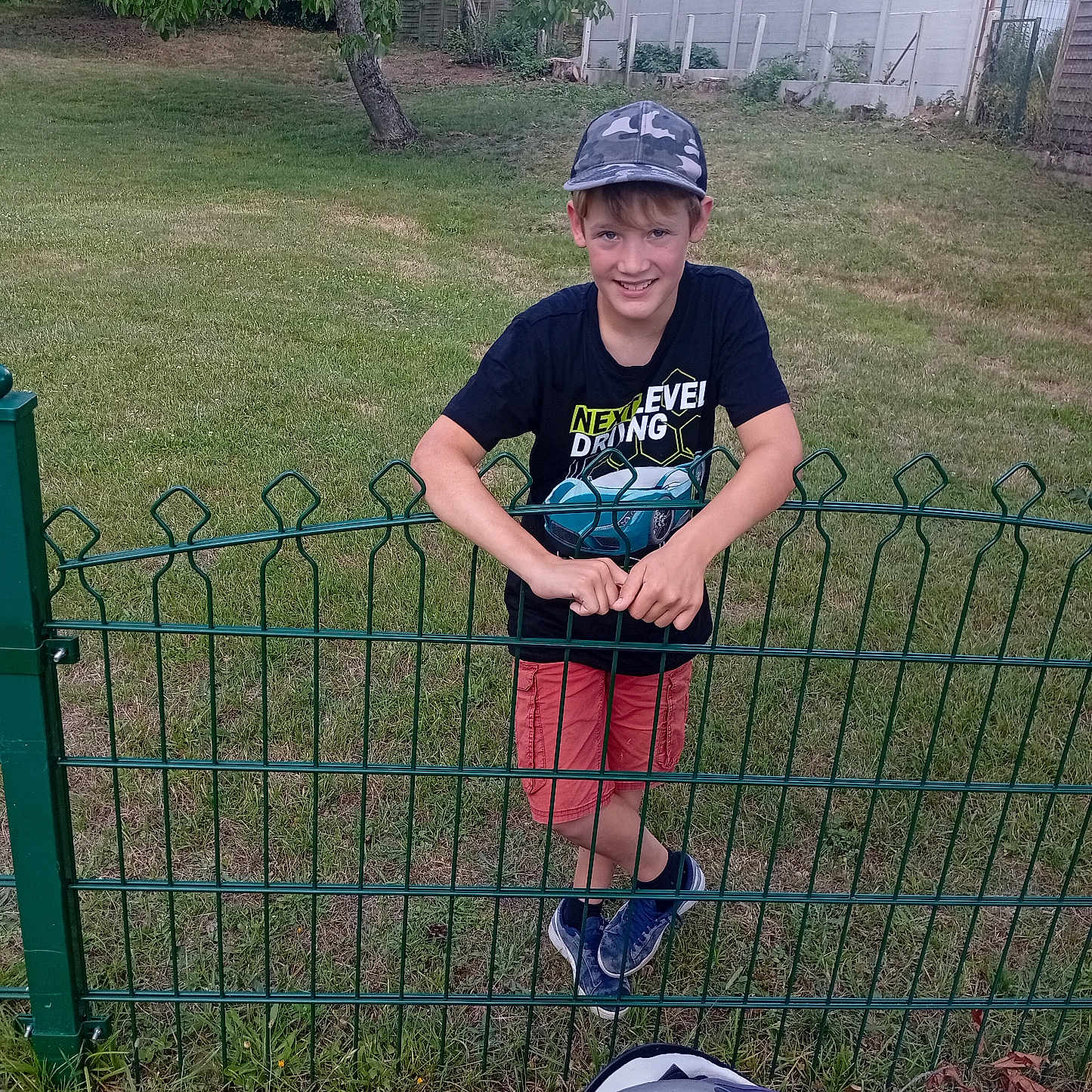 Enzo a rejoint le concours — aidez-le/la à gagner de superbes lots ! backyard, badminton, boy, cap, casual_wear, child, fence, grass, happy, outdoor, person, play, recreation, shorts, shuttlecock, smiling, sports_equipment, summer, tree, tshirt