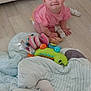 baby, blanket, child, colorful, couch, crawling, cute, floor, happy, head, indoor, infant, person, pink_shirt, playful, smiling, sock, soft_toys, toys, wooden_floor