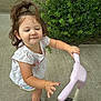 Millie is registered to the contest to win money with this photo: toddler, child, scooter, outdoor, sidewalk, greenery, plant, shrub, white_shirt, shorts, sandals, play, fun, smile, person, hair_tie, cute, summer, daylight, footwear