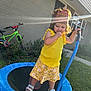 Millie joined the competition — help win amazing prizes! child, girl, yellow_clothing, birthday_crown, trampoline, outdoor, grass, bicycle, house, sunflare, summer, play, happy, footwear, sidewalk, window, greenery, toy, daylight, portrait