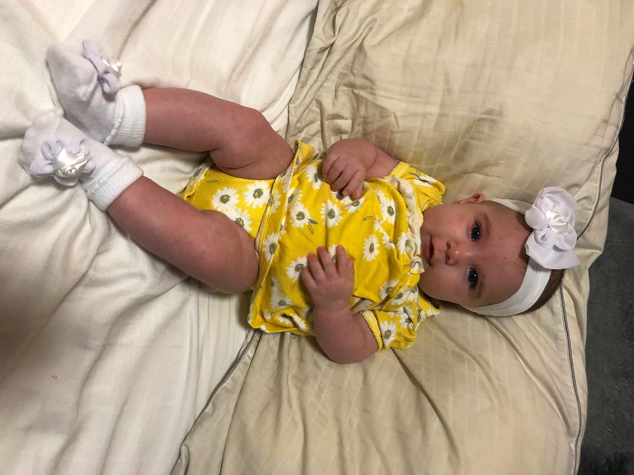 Harper is registered to the contest to win money with this photo: baby, baby_products, baby_safety, baby_sleeping, baby_toddler_clothing, child, comfort, finger, gesture, hand, headwear, human_body, jewellery, linens, person, room, sitting, skin, sleeve, textile