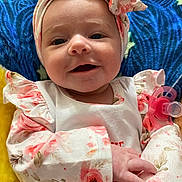 Coraline is registered to the contest to win money with this photo: baby, child, smiling, headband, floral, clothing, pacifier, blanket, cute, infant, portrait, happy, young, lying_down, closeup, person, soft, colorful, indoors, hand