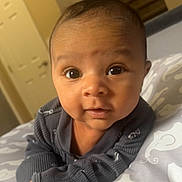 Zion is registered to the contest to win money with this photo: baby, bed, blanket, child, cozy, curious, cute, elephant_pattern, expression, eyes, face, indoors, infant, lying_down, pajamas, person, portrait, sleepwear, soft_light, young