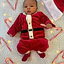 Zion is registered to the contest to win money with this photo: baby, blanket, candy_cane, celebration, child, christmas, cozy, cute, fairy_lights, festive, heart_shape, holding_object, holiday, indoors, infant, lying_down, red_clothing, santa_outfit, smiling, soft_texture