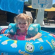 Kelsey is registered to the contest to win money with this photo: basketball_hoop, blue, cartoon_characters, child, cute, daytime, floatation_device, happy, inflatable_ring, lawn_chair, outdoor, patio, pigtails, playful, pool, smiling, summer, sunny, swimming, water