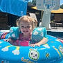 child, pool, inflatable_ring, swimming, water, summer, outdoor, sunny, pigtails, smiling, floatation_device, cartoon_characters, basketball_hoop, patio, lawn_chair, blue, cute, happy, playful, daytime