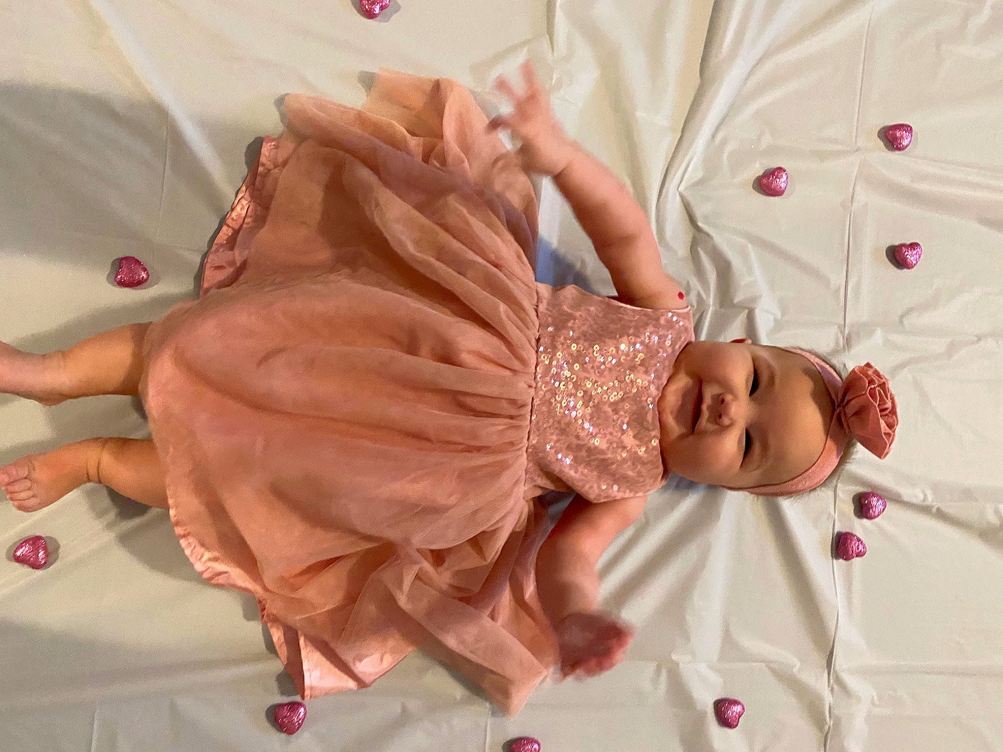 Elliana is registered to the contest to win money with this photo: baby, baby_products, baby_toddler_clothing, child, comfort, dress, event, gesture, hand, happy, head, headwear, jewellery, linens, peach, person, pink, room, satin, sleeve