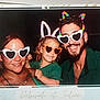 adult, beard, bunny_ears, casual_clothing, child, colorful_ears, curly_hair, dark_background, earrings, family, fun, glasses, green_clothing, happy, headband, heart_shaped_glasses, party, photo_booth, portrait, smile