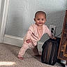 baby, infant, child, standing, pink_onesie, carpet, file_organizer, furniture, wall, power_outlet, smiling, indoor, home, curious, barefoot, person, head, face, hand, support