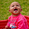 Alora is registered to the contest to win money with this photo: baby, child, pink_sweater, smiling, happy, outdoor, grass, red_seat, cute, portrait, infant, casual_clothing, playful, sitting, young_child, cheerful, bright_colors, looking_up, joyful, daylight