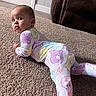 baby, child, pajamas, carpet, floor, living_room, couch, furniture, person, face, head, expression, curious, indoors, home, colorful, pattern, sleepwear, cute, lying_down