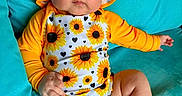 Sabrina is registered to the contest to win money with this photo: baby, child, sunflower, hat, yellow, orange, blue_couch, infant, clothing, portrait, cute, indoors, sitting, one_person, face, skin, legs, hand, foot, expression