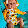 baby, child, sunflower, hat, yellow, orange, blue_couch, infant, clothing, portrait, cute, indoors, sitting, one_person, face, skin, legs, hand, foot, expression